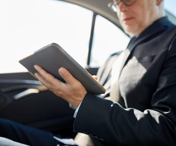 transport, business trip, technology and people concept - senior businessman with tablet pc computer driving on car back seat